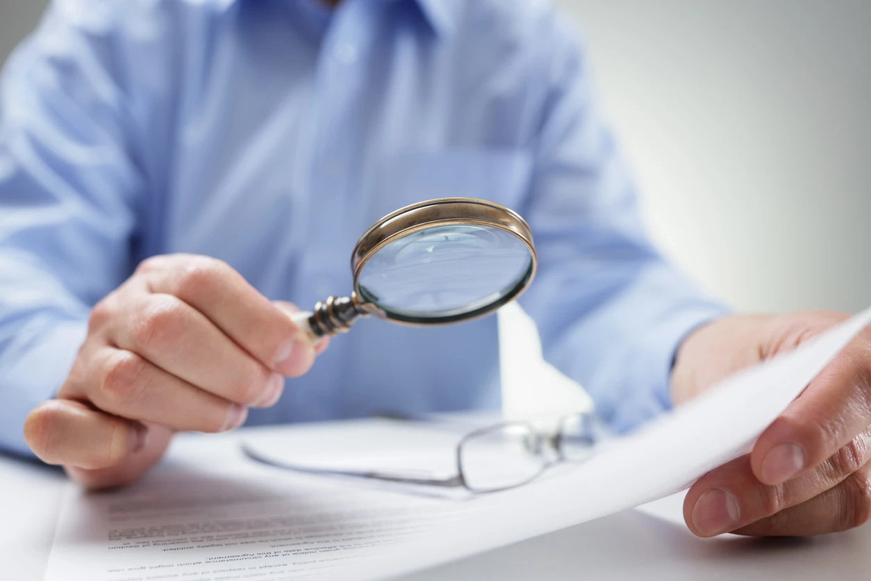 Man holding up a magnifying glass to a document.