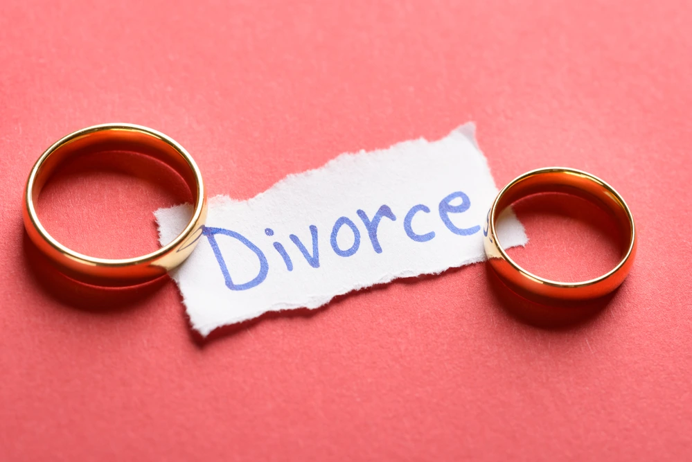 Divorce written out on a piece of paper and two gold wedding bands.