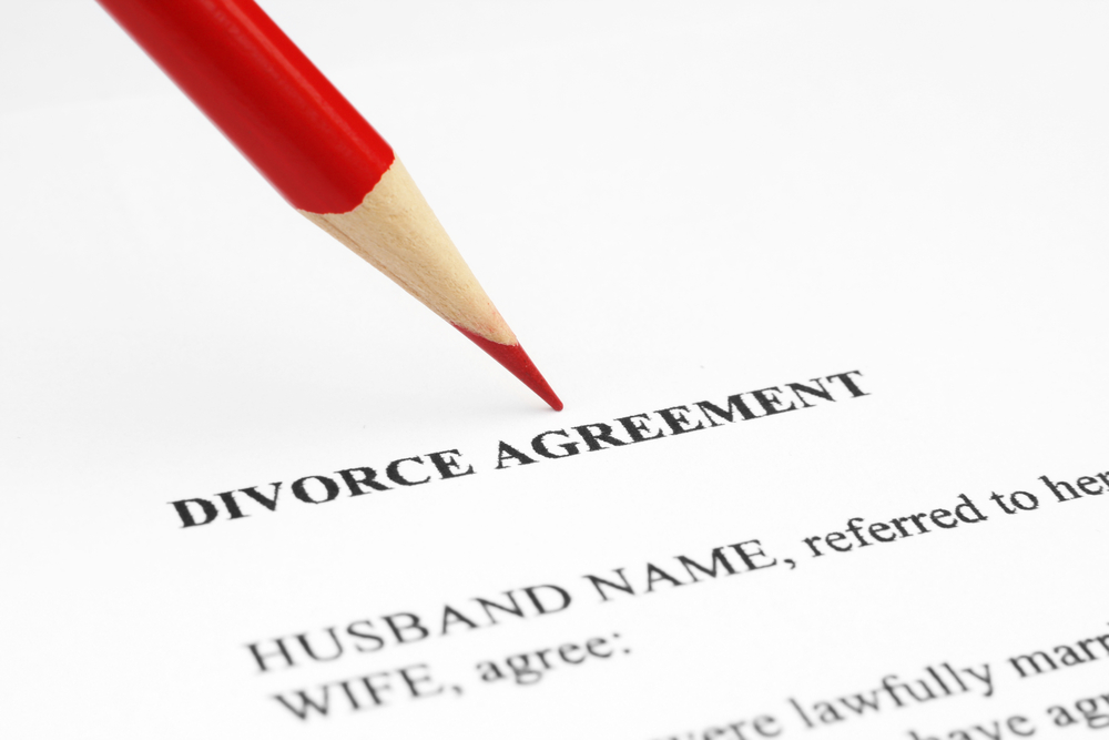 Red pencil pointing at the words "divorce agreement" written on paper.