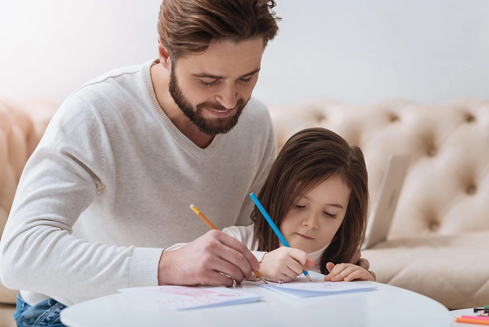 Man sits next to his child at a table as they both write on paper together. Our Houston father's rights lawyers fight to preserve the legal rights of any father who wants to continue seeing their children.
