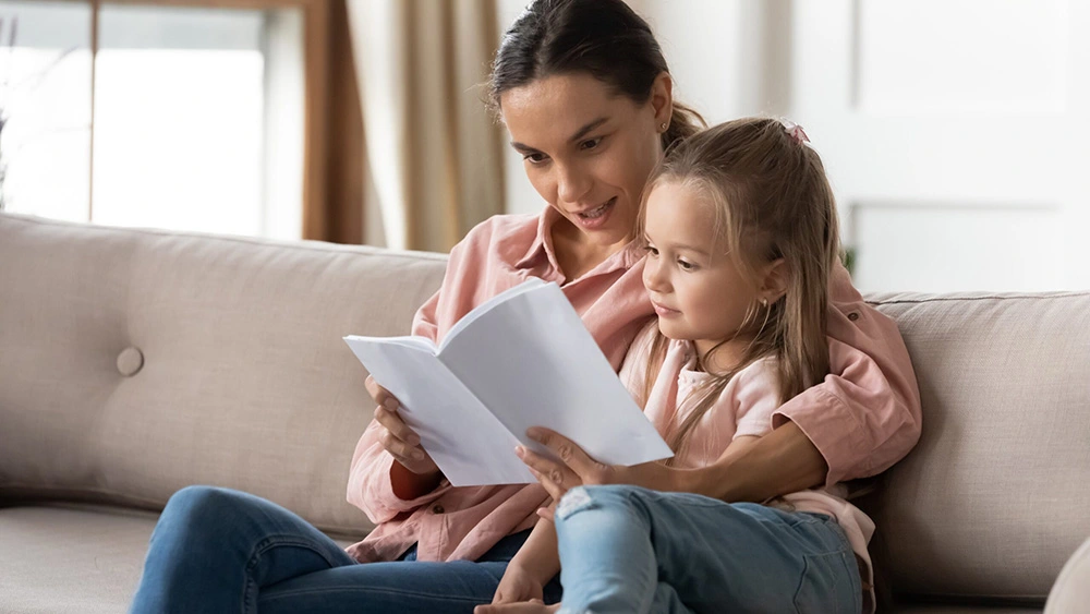 Woman sits with arm around child on couch as they read a book together. Our Houston women’s rights lawyers aim to provide the best legal support to protect every mothers’ rights.