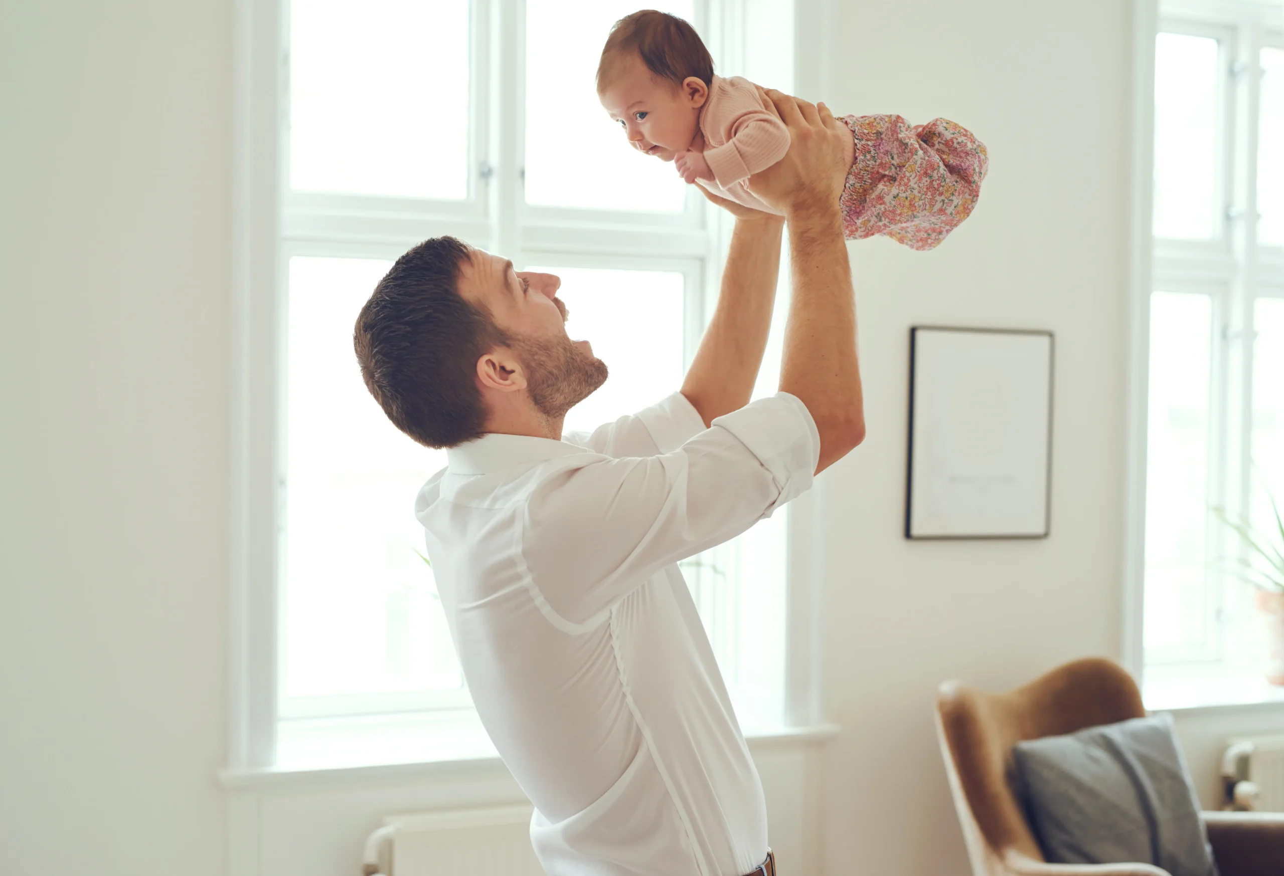 Father holding small baby in the air and smiling.